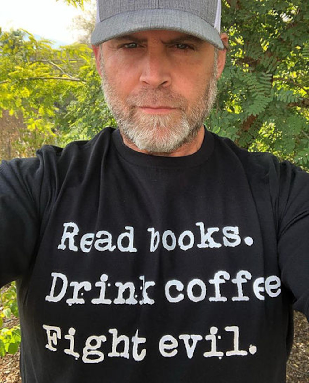 An image of Chris Baron. He wears a gray hat and a black shirt that reads "Read books. Drink coffee. Fight evil."