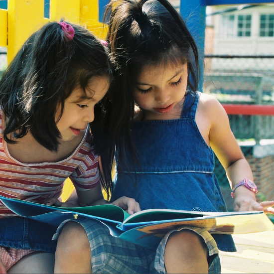 Girls sharing a book reading moment on playground